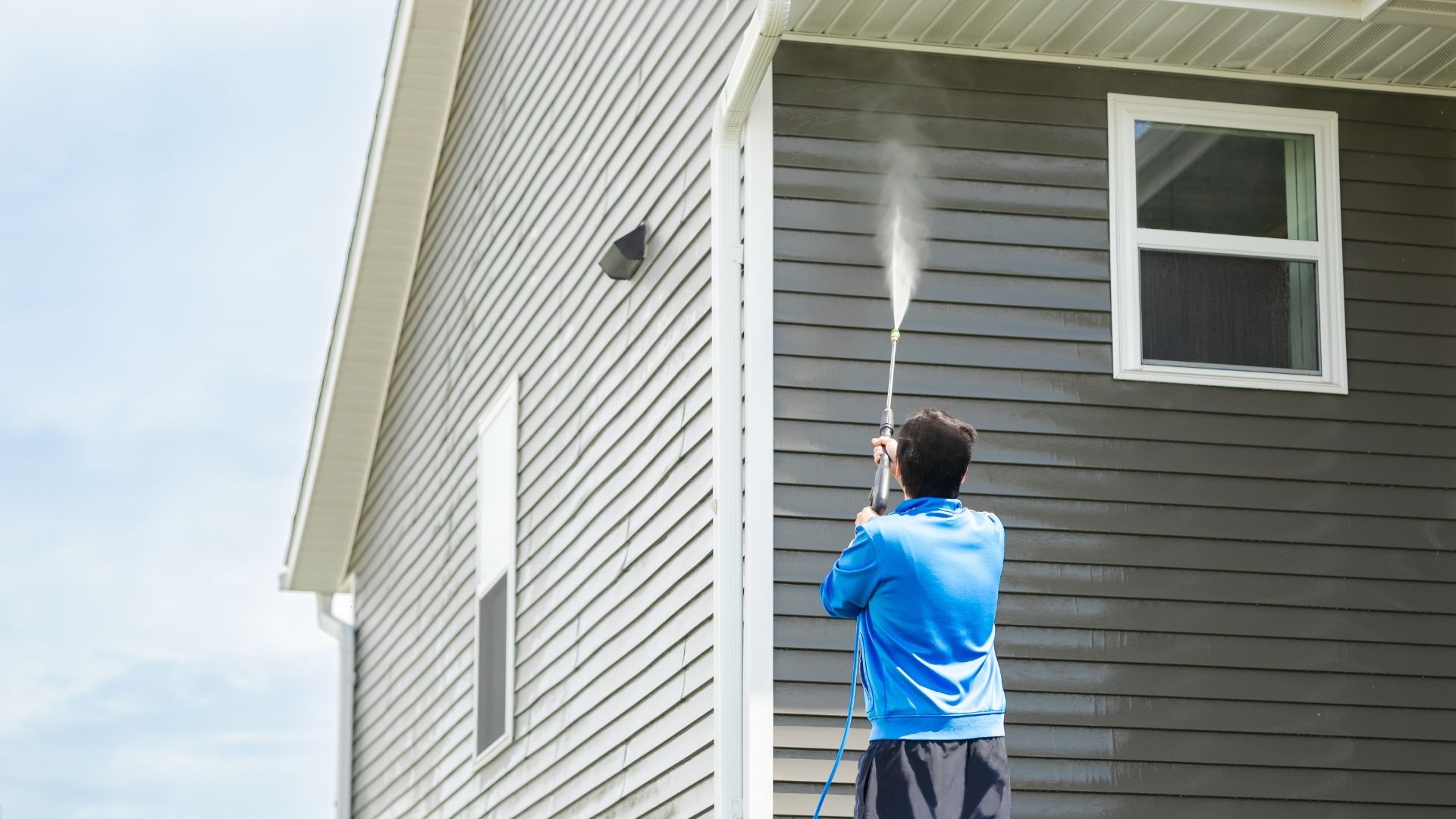 professional pressure washing siding of gray home