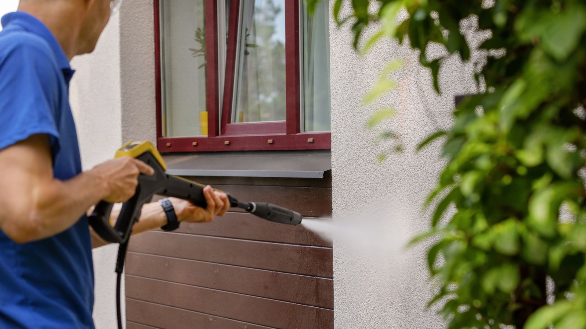 professional pressure washing siding of brown home