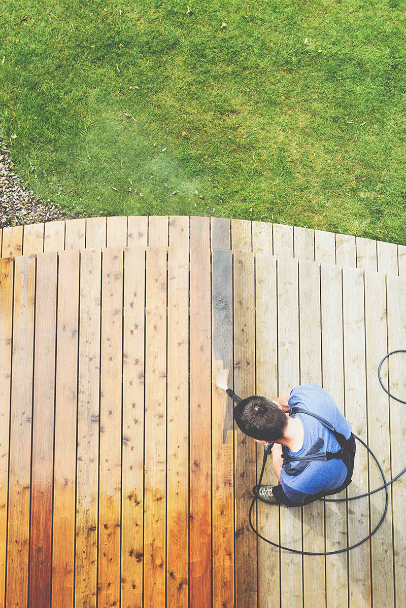 professional in blue shirt pressure washing wooden deck